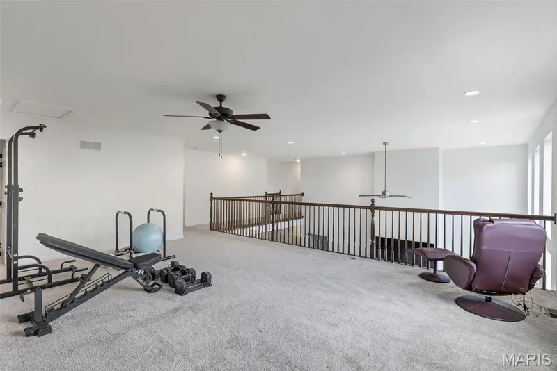 Spacious open loft area with carpeted flooring, two ceiling fans, recessed lighting, and a dark wood-finish railing — 337 White Orchid Court, Wentzville, MO 63385