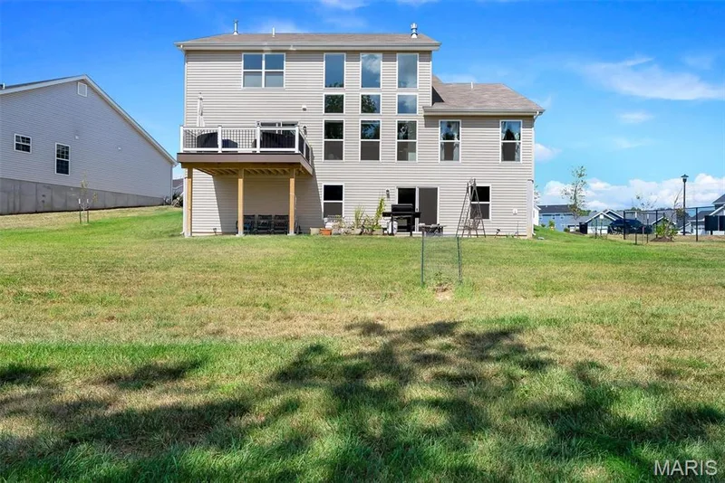 Expansive green space surrounds the property, featuring a raised deck with white railings and an exterior door, alongside multiple windows, including a prominent window wall — 337 White Orchid Court, Wentzville, MO 63385