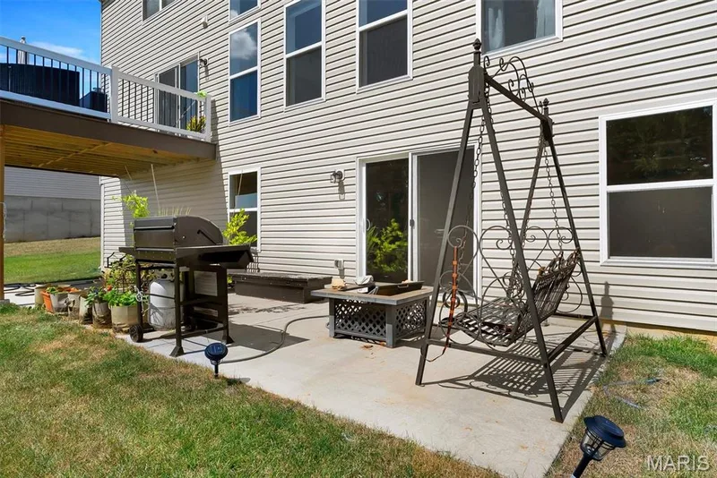 Ground-level patio with concrete surfacing, siding exterior, sliding glass door access, and an upper-level deck with white railings — 337 White Orchid Court, Wentzville, MO 63385