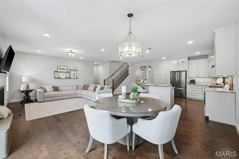 Open-concept living area featuring rich wood-finish flooring, a contemporary kitchen with light cabinetry and stainless steel appliances, and a dining area illuminated by a decorative chandelier — 140 Oakleigh Park Lane, St Charles, MO 63303