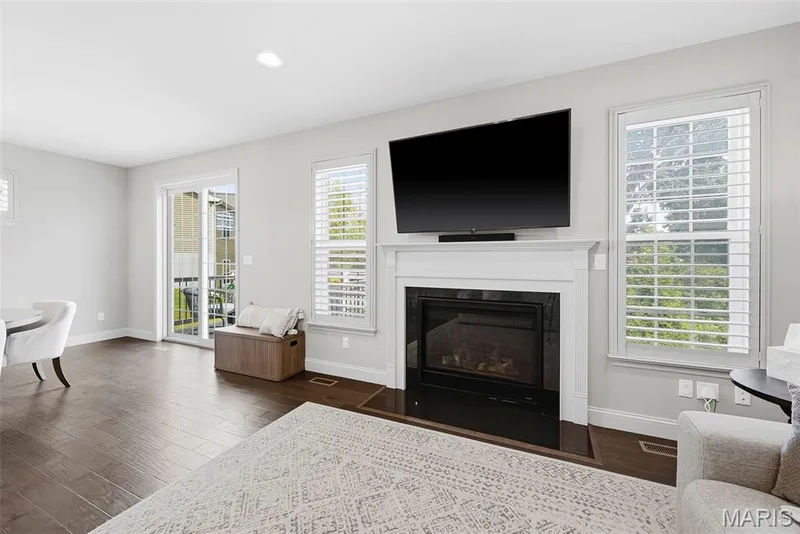 Wood-finish flooring throughout, gas fireplace with a classic mantel, recessed lighting, and a sliding glass door to an outdoor space. Shutters through out the first floor — 140 Oakleigh Park Lane, St Charles, MO 63303