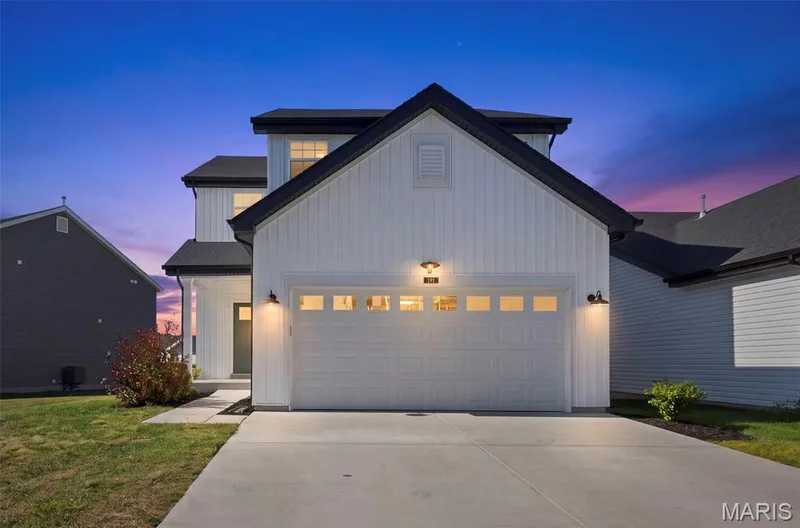 Two-story residence featuring vertical white siding, black-trimmed windows, a two-car garage with transom windows, and a paved driveway — 191 Crestfield Court, St Charles, MO 63301