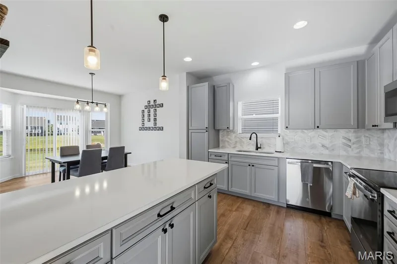 Modern kitchen featuring a large center island, gray cabinetry, stainless steel appliances, and wood-finish flooring — 191 Crestfield Court, St Charles, MO 63301