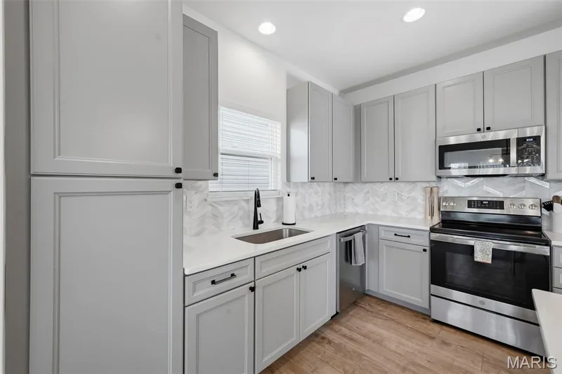 Kitchen featuring light gray cabinetry, stainless steel appliances, a white solid surface countertop, a patterned backsplash, and wood-finish flooring — 191 Crestfield Court, St Charles, MO 63301