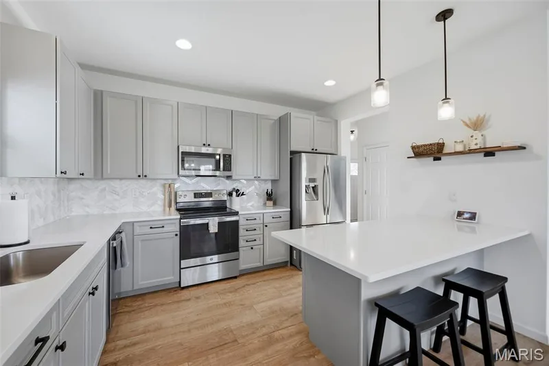 Modern kitchen featuring light gray cabinetry, stainless steel appliances, white countertops, and wood-finish flooring — 191 Crestfield Court, St Charles, MO 63301