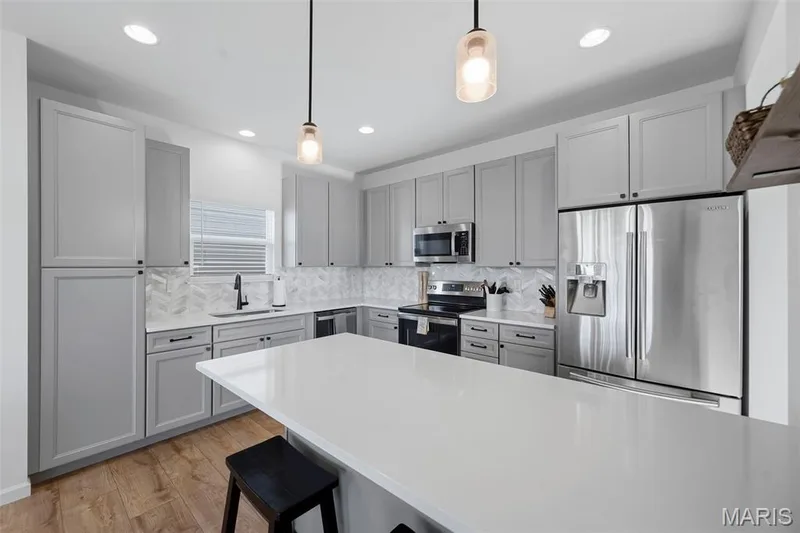 Modern kitchen featuring a large center island, white countertops, gray cabinetry, and stainless steel appliances — 191 Crestfield Court, St Charles, MO 63301