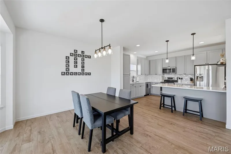 Open-concept layout featuring wood-finish flooring, a kitchen island with seating, pendant lighting, and stainless steel appliances — 191 Crestfield Court, St Charles, MO 63301