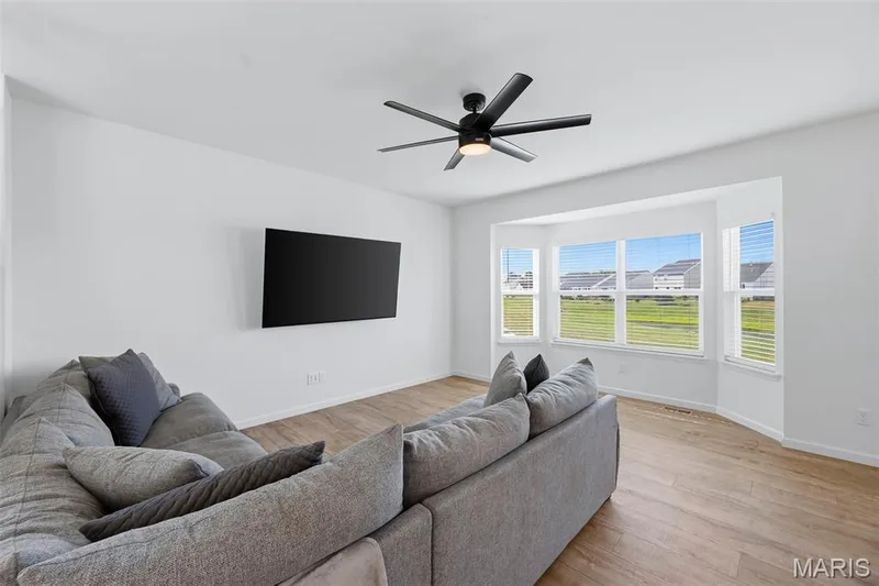 Wood-finish flooring, white walls, bay window with blinds, and a ceiling fan with integrated lighting — 191 Crestfield Court, St Charles, MO 63301