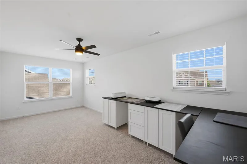 Carpeted room featuring multiple windows, a ceiling fan, and built-in cabinetry with dark countertops — 191 Crestfield Court, St Charles, MO 63301