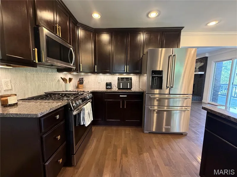 Rich dark wood cabinetry, stainless steel appliances, wood-finish flooring, light-toned backsplash, and recessed lighting — 584 Sunbridge Drive, Chesterfield, MO 63017