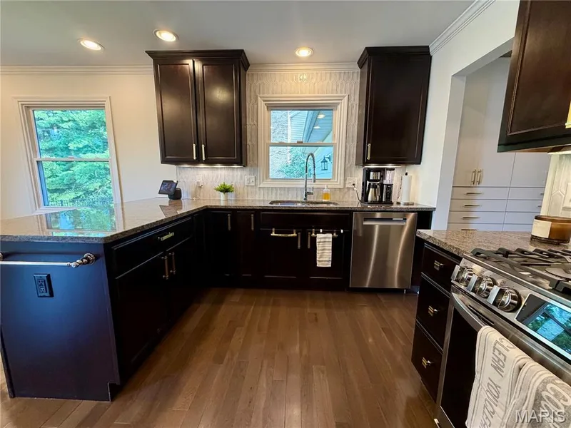 Dark wood cabinetry with gold-tone hardware, stainless steel appliances, granite countertops, and wood-finish flooring — 584 Sunbridge Drive, Chesterfield, MO 63017