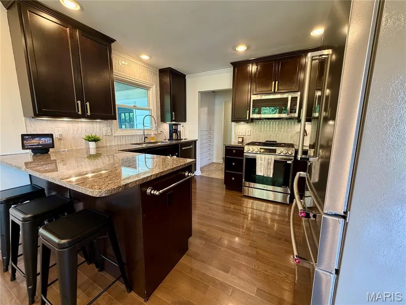 Kitchen featuring dark wood cabinetry, light-toned backsplash, stainless steel appliances, and a granite-topped island with seating — 584 Sunbridge Drive, Chesterfield, MO 63017