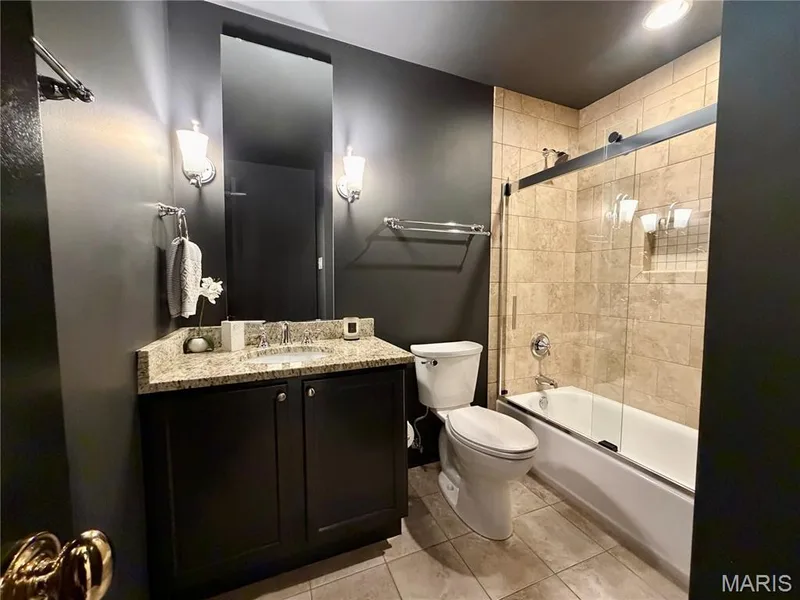 Full bathroom featuring a single vanity with stone-finish countertop, dark wood-finish cabinetry, and a shower-tub combination with a glass enclosure — 584 Sunbridge Drive, Chesterfield, MO 63017