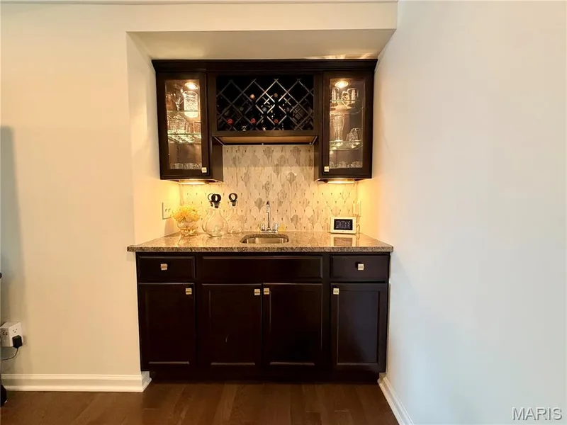 Built-in wet bar featuring dark wood-finish cabinetry, granite countertop, undermount sink, and mosaic tile backsplash — 584 Sunbridge Drive, Chesterfield, MO 63017