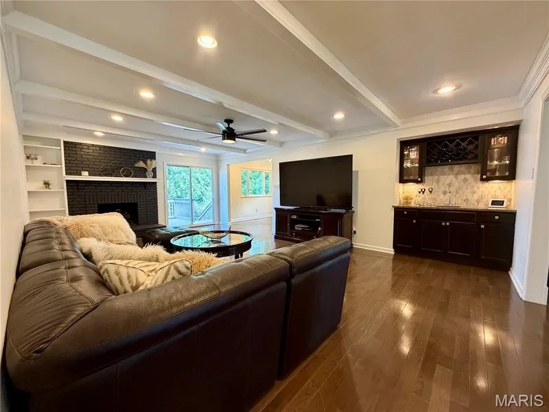 Coffered ceiling with recessed lighting, integrated built-in shelving, a fireplace with a black brick surround and mantel, rich wood-finish flooring, and a built-in wet bar with cabinetry and a wine rack — 584 Sunbridge Drive, Chesterfield, MO 63017