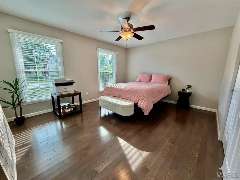 Hardwood flooring, two windows with blinds, ceiling fan with integrated lighting, and neutral wall paint — 584 Sunbridge Drive, Chesterfield, MO 63017