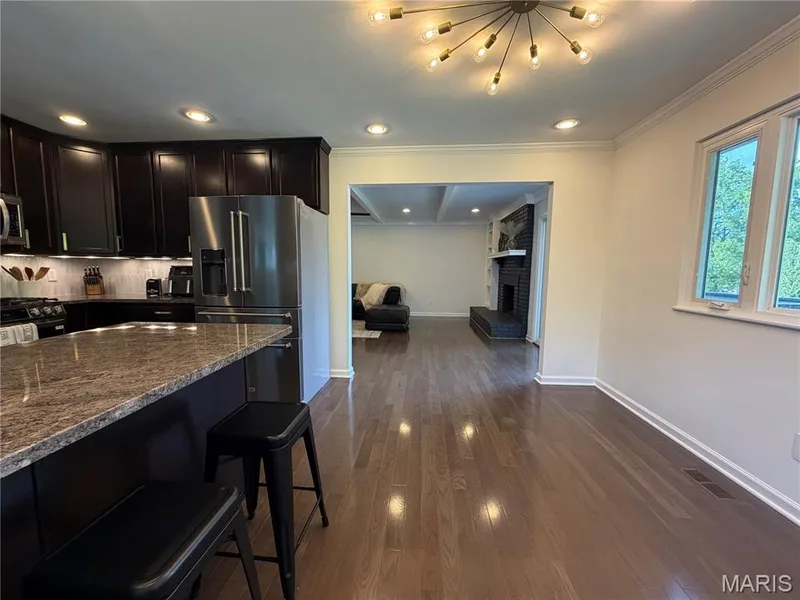 Wood-finish flooring throughout, with a kitchen featuring dark wood cabinetry, a stone countertop island, and stainless steel appliances — 584 Sunbridge Drive, Chesterfield, MO 63017