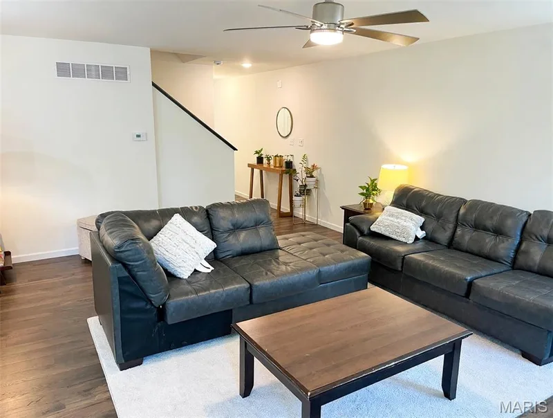 Wood-finish flooring throughout, featuring a ceiling fan with integrated lighting, and a staircase with a dark handrail — 157 Day Lily Lane, Wentzville, MO 63385
