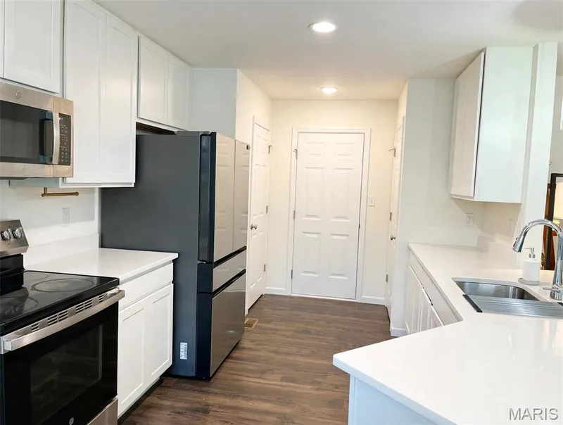 White cabinetry with sleek hardware, stainless steel appliances, wood-finish flooring, white countertops, and recessed lighting — 157 Day Lily Lane, Wentzville, MO 63385