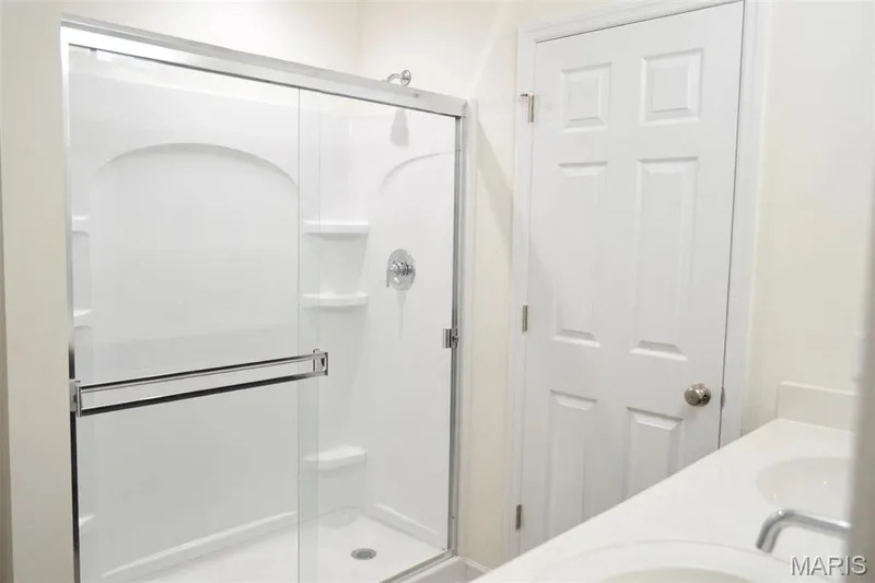 White shower enclosure with clear glass sliding door, integrated shelving, chrome fixtures, and a six-panel interior door — 157 Day Lily Lane, Wentzville, MO 63385