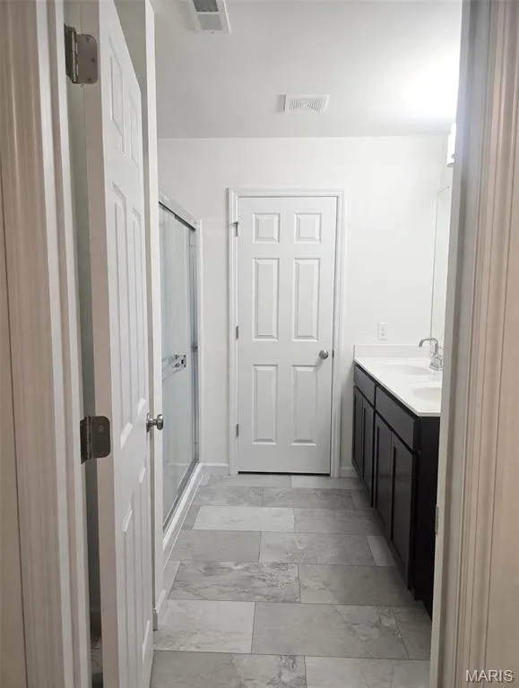 Grey-toned tiled flooring, dark wood-finish vanity with dual sinks, white countertops, and a glass-enclosed shower — 157 Day Lily Lane, Wentzville, MO 63385