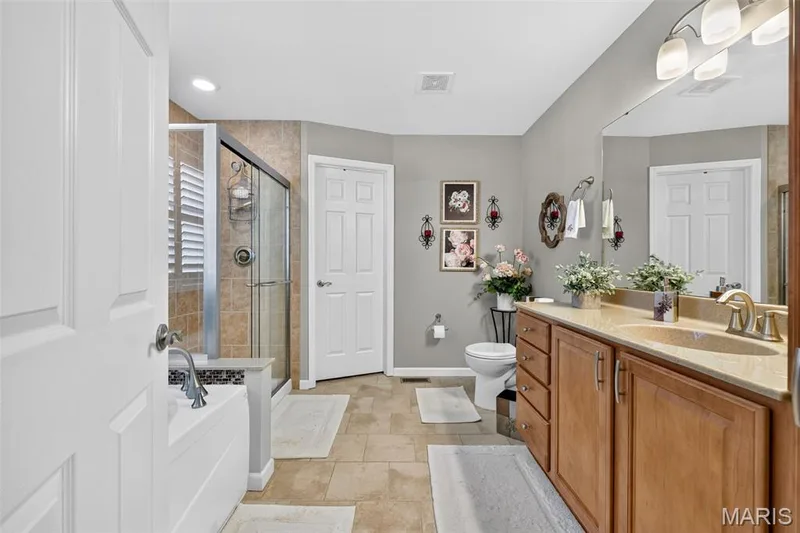 Neutral-toned tile flooring, dual-sink vanity with wood-finish cabinetry, built-in bathtub, glass-enclosed shower, and recessed lighting — 29 Edenshire Court #69B, Dardenne Prairie, MO 63368