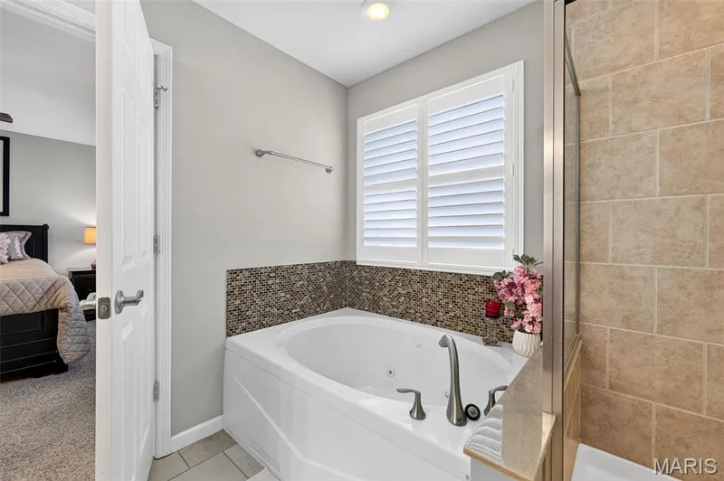 Corner soaking tub with mosaic tile surround, window with white plantation shutters, and a tiled shower enclosure — 29 Edenshire Court #69B, Dardenne Prairie, MO 63368