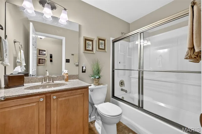 Bathroom featuring a wood-finish vanity with an integrated sink, a granite-look countertop, a built-in mirror, and a shower-over-tub with sliding glass doors — 29 Edenshire Court #69B, Dardenne Prairie, MO 63368