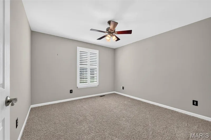 Carpeted room with a ceiling fan, window with white plantation shutters, and light gray wall paint — 29 Edenshire Court #69B, Dardenne Prairie, MO 63368
