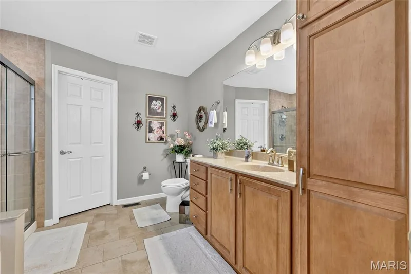 Dual-sink vanity with light wood-finish cabinetry, neutral countertop, and large mirror — 29 Edenshire Court #69B, Dardenne Prairie, MO 63368
