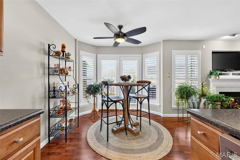 Bay window with plantation shutters, wood-finish flooring, ceiling fan, and built-in fireplace with mantel — 29 Edenshire Court #69B, Dardenne Prairie, MO 63368