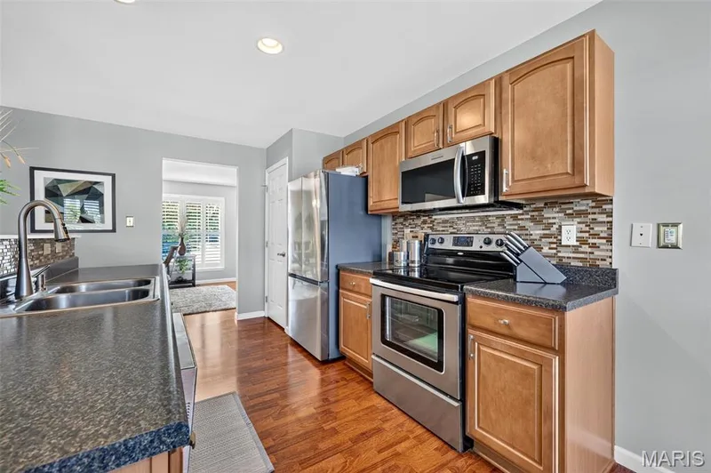 Wood-finish flooring, stainless steel appliances, granite-style countertops, wood cabinetry, and a mosaic tile backsplash — 29 Edenshire Court #69B, Dardenne Prairie, MO 63368