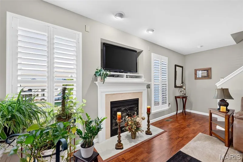 Fireplace with a stone surround and a classic mantel, wood-finish flooring, white plantation shutters, recessed ceiling lighting, and a white staircase with a railing — 29 Edenshire Court #69B, Dardenne Prairie, MO 63368