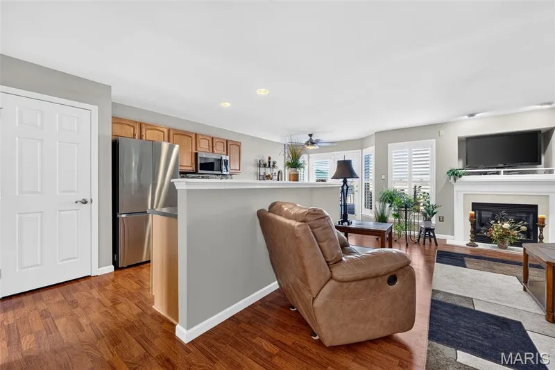 Wood-finish flooring throughout, featuring a fireplace with a white mantel, stainless steel refrigerator, and wood cabinetry — 29 Edenshire Court #69B, Dardenne Prairie, MO 63368