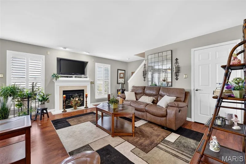 Hardwood-finish flooring throughout, featuring a fireplace with a stone surround and white mantle, and white plantation shutters on windows — 29 Edenshire Court #69B, Dardenne Prairie, MO 63368