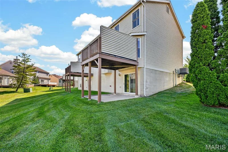 Expansive green space featuring elevated decks, a ground-level concrete patio, a sliding glass door, and established perimeter plantings — 29 Edenshire Court #69B, Dardenne Prairie, MO 63368