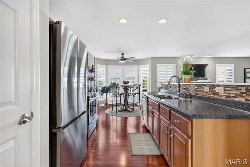 Kitchen featuring stainless steel appliances, dark wood-finish flooring, a mosaic tile backsplash, and a breakfast bar with stone countertops — 29 Edenshire Court #69B, Dardenne Prairie, MO 63368