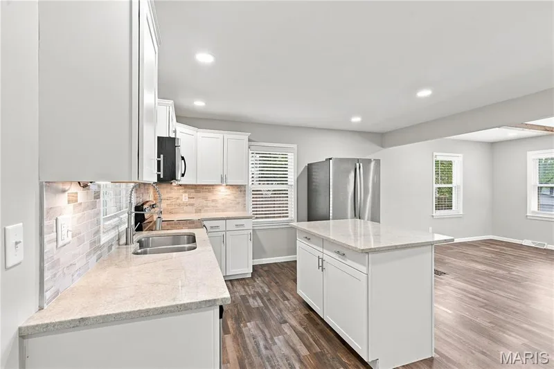 Kitchen featuring light-toned cabinetry, light-toned countertops, tile backsplash, stainless steel sink, and wood-finish flooring — 1620 Dale Avenue, St Charles, MO 63301
