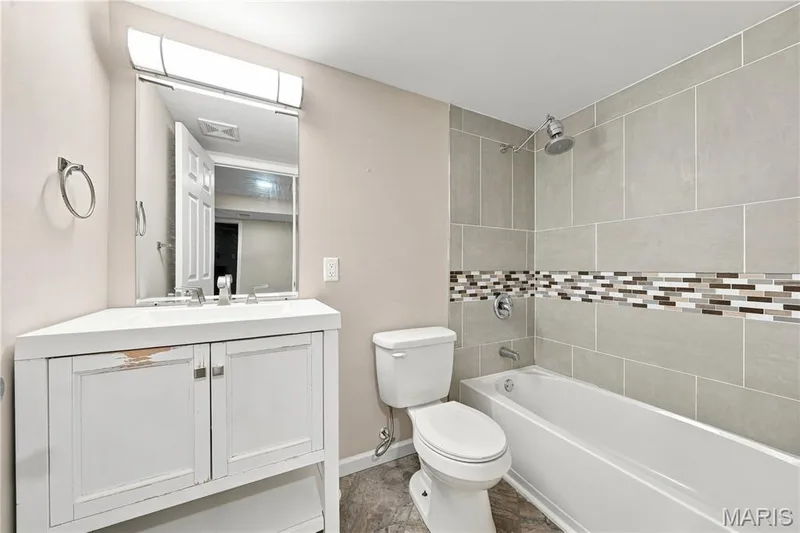 Lower level Bathroom featuring a white vanity with an integrated sink, rectangular mirror with overhead lighting, a white toilet, and a shower-tub — 1620 Dale Avenue, St Charles, MO 63301