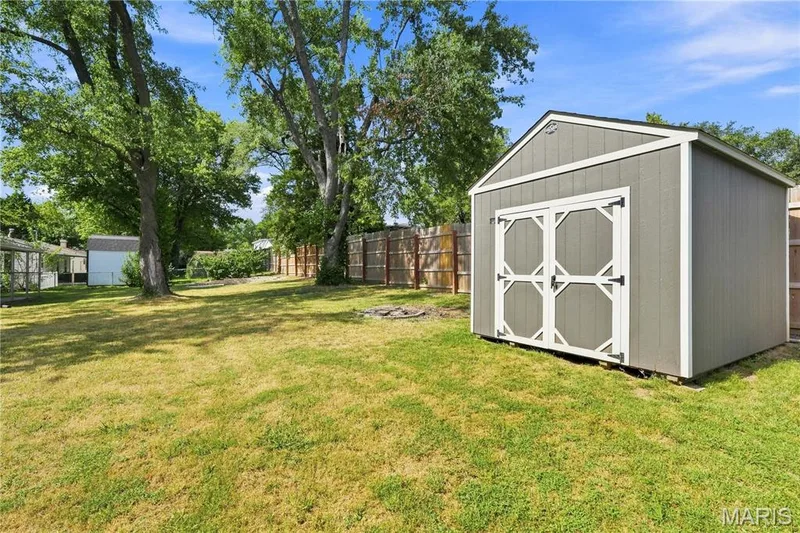 Expansive backyard with mature shade trees and level lawn, complemented by a detached storage shed featuring gray board-and-batten siding, white trim accents, and geometric door paneling — 1620 Dale Avenue, St Charles, MO 63301