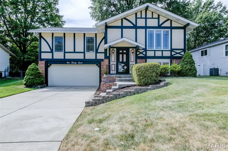 Split-level residence featuring a two-car garage, concrete driveway, and a brick retaining wall — 127 Spring Leaf Drive, St Peters, MO 63376
