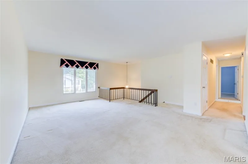 Carpeted living space with a large window, a wood and wrought iron railing, and a hallway with flush-mount lighting — 127 Spring Leaf Drive, St Peters, MO 63376