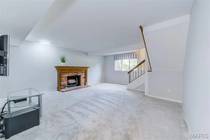 Spacious room featuring light-toned carpeting, a brick fireplace with a wood mantle, and a white staircase with a wood handrail — 127 Spring Leaf Drive, St Peters, MO 63376
