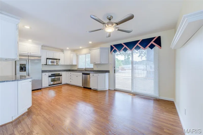 White cabinetry, granite countertops, stainless steel appliances, wood-finish flooring, and a sliding glass door — 127 Spring Leaf Drive, St Peters, MO 63376