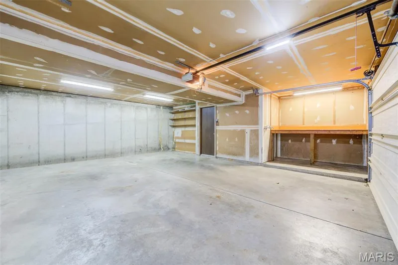 Spacious 2 car garage featuring concrete flooring, built-in shelving, a workbench, and overhead lighting — 127 Spring Leaf Drive, St Peters, MO 63376