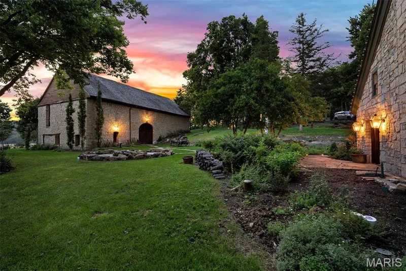 Stone exterior building with dark roof, manicured lawn, established landscaping, and exterior wall lanterns — 2275 Highway F, Defiance, MO 63341