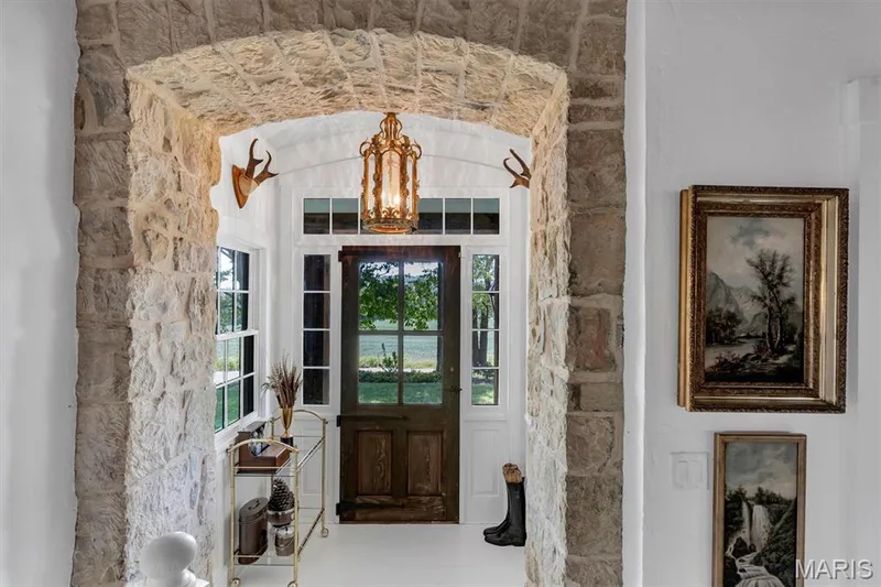 Stone archway entryway with a wood-panel door, transom window, side windows, and an ornate ceiling fixture — 2275 Highway F, Defiance, MO 63341
