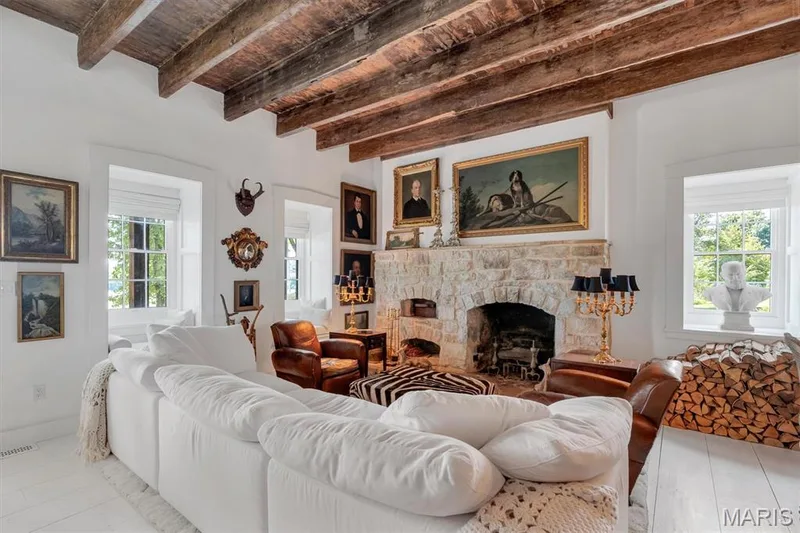 Exposed wood beam ceiling, stone-faced fireplace, white painted wood-finish flooring, white window frames, and built-in firewood storage — 2275 Highway F, Defiance, MO 63341