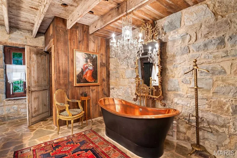 Stone wall accents, exposed wood beam ceiling, freestanding copper bathtub, decorative wall mirror, and wood-paneled walls — 2275 Highway F, Defiance, MO 63341