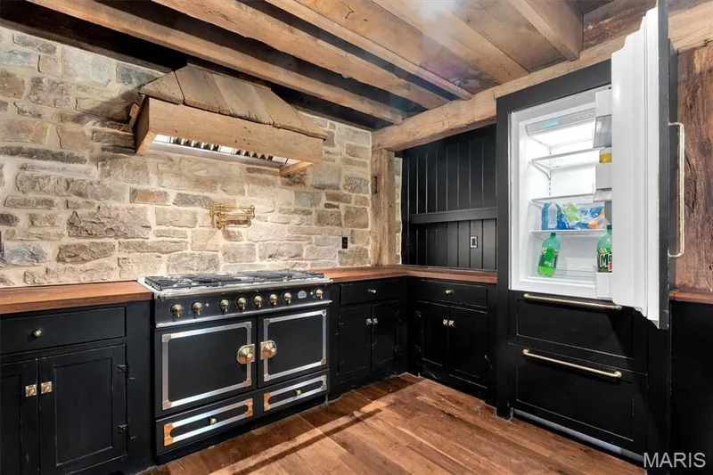 Exposed wood beam ceiling, stone wall, built-in range hood, dark wood-finish countertops, and black cabinetry — 2275 Highway F, Defiance, MO 63341